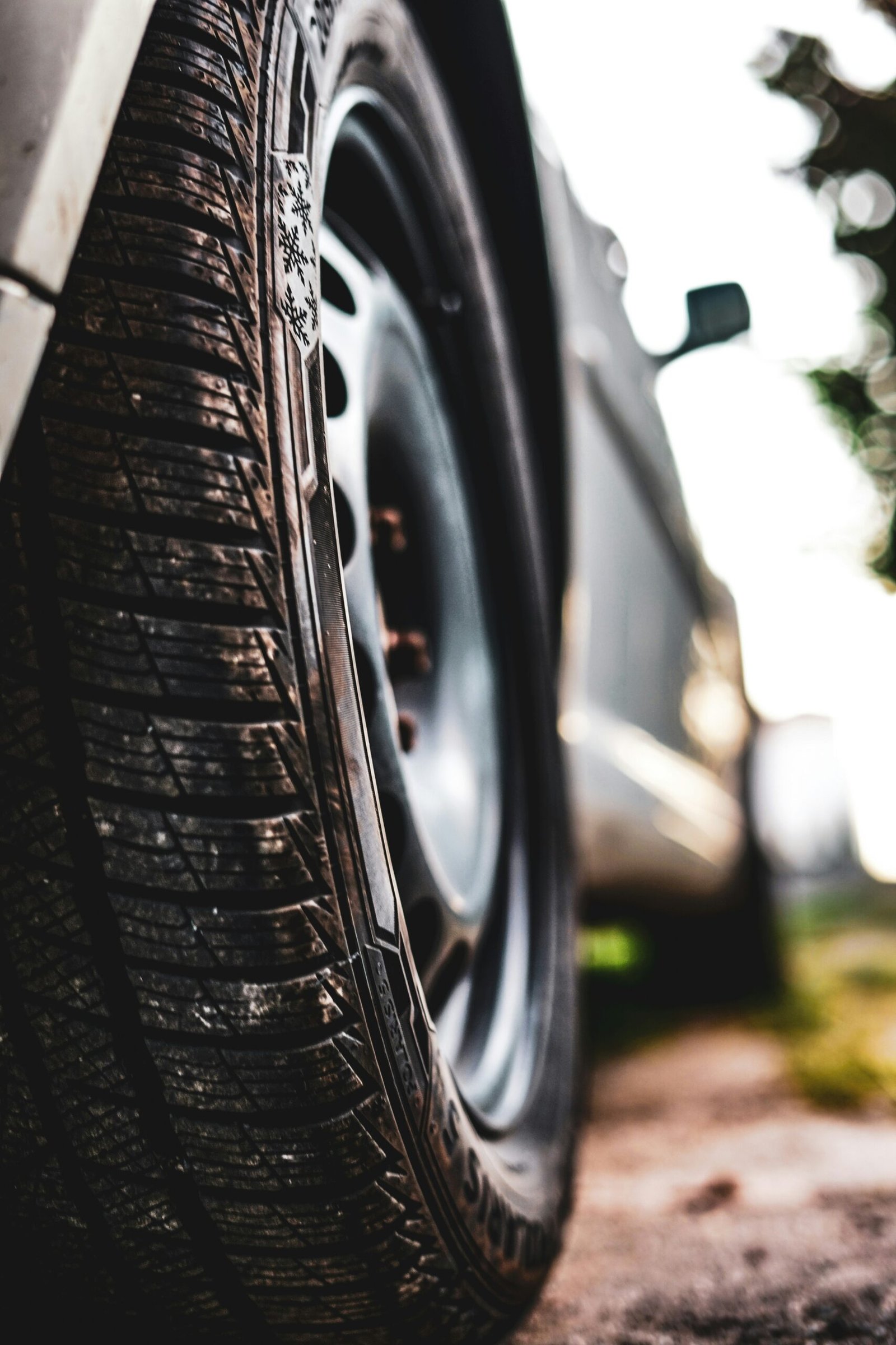 Close-up view of a car tire showing detailed tread patterns and a snowflake symbol, with the vehicle and background softly blurred.

